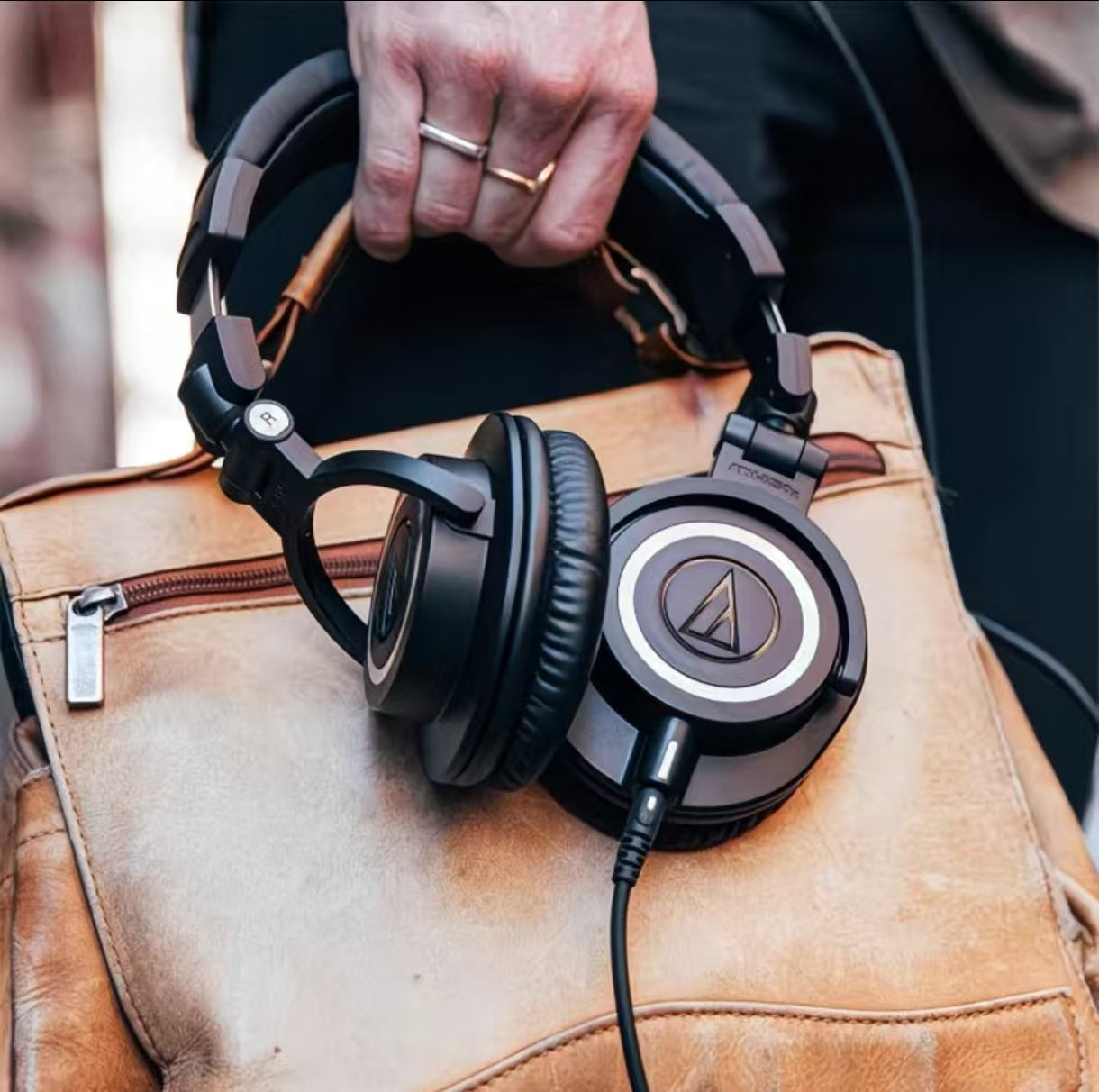 Audio-Technica ATH-M50xENSO headphones placed on a brown leather bag — showcasing durable metal frame, soft earpads, and wired connection perfect for studio and daily use.