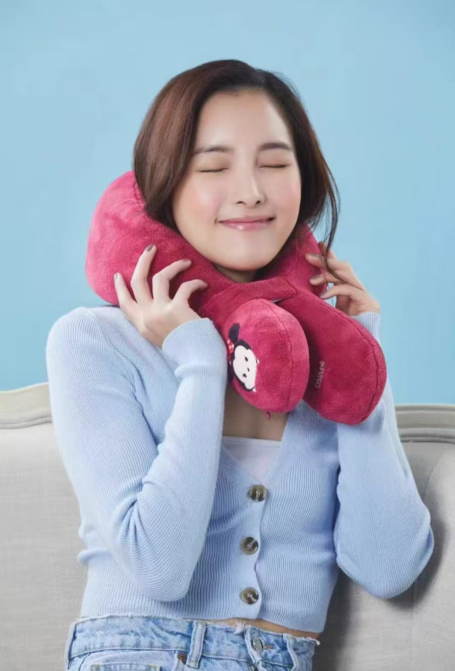 A woman wearing the red OSIM uSnooz massage wrap with Minnie Mouse faces around her neck, enjoying relaxation. The soft, ergonomic design supports the neck and shoulders comfortably.