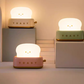 Three toaster night lights in white, green and pink on grey display plinths showing the available colour options