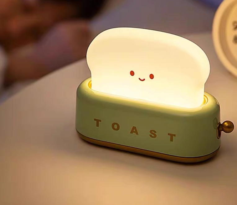 Green toaster night light glowing on bedside table beside sleeping person for soft sleep-friendly bedroom lighting